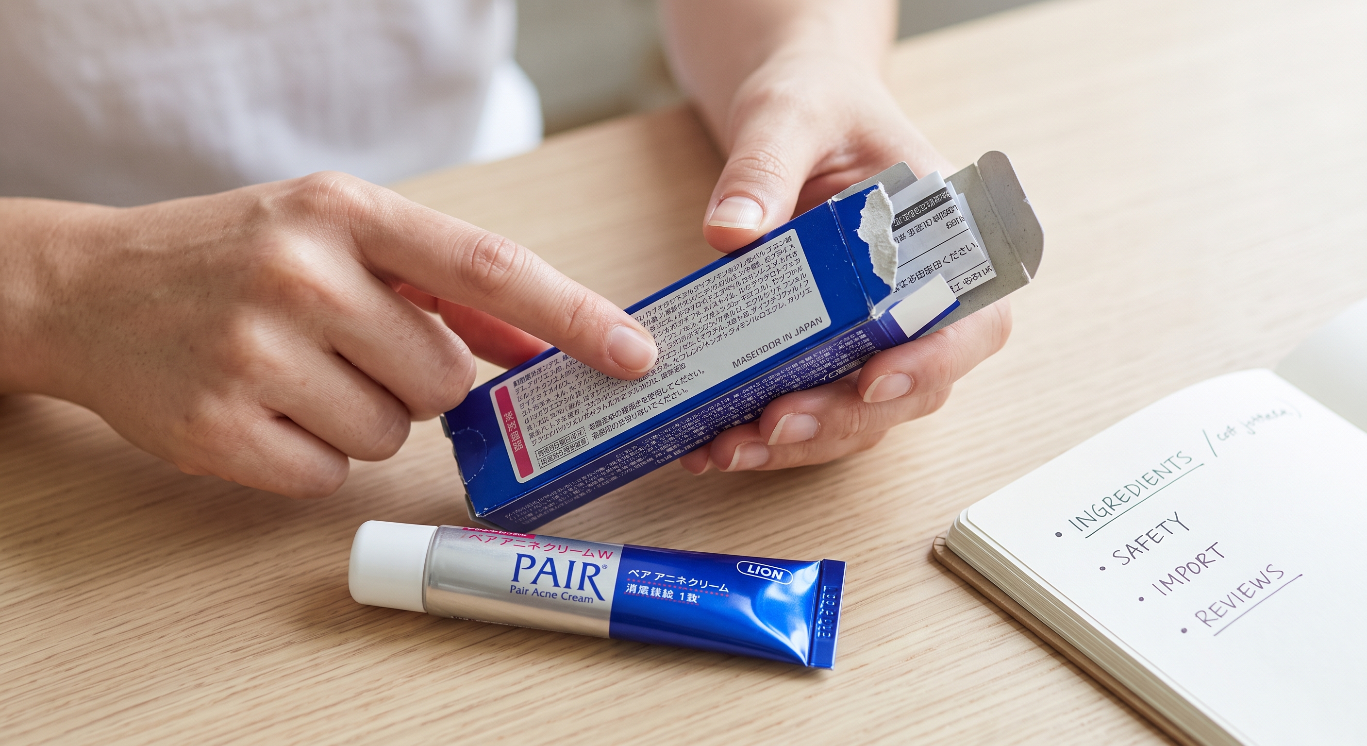 A person holding a Japanese acne cream box, pointing at ingredient details beside an open tube and a safety checklist.
