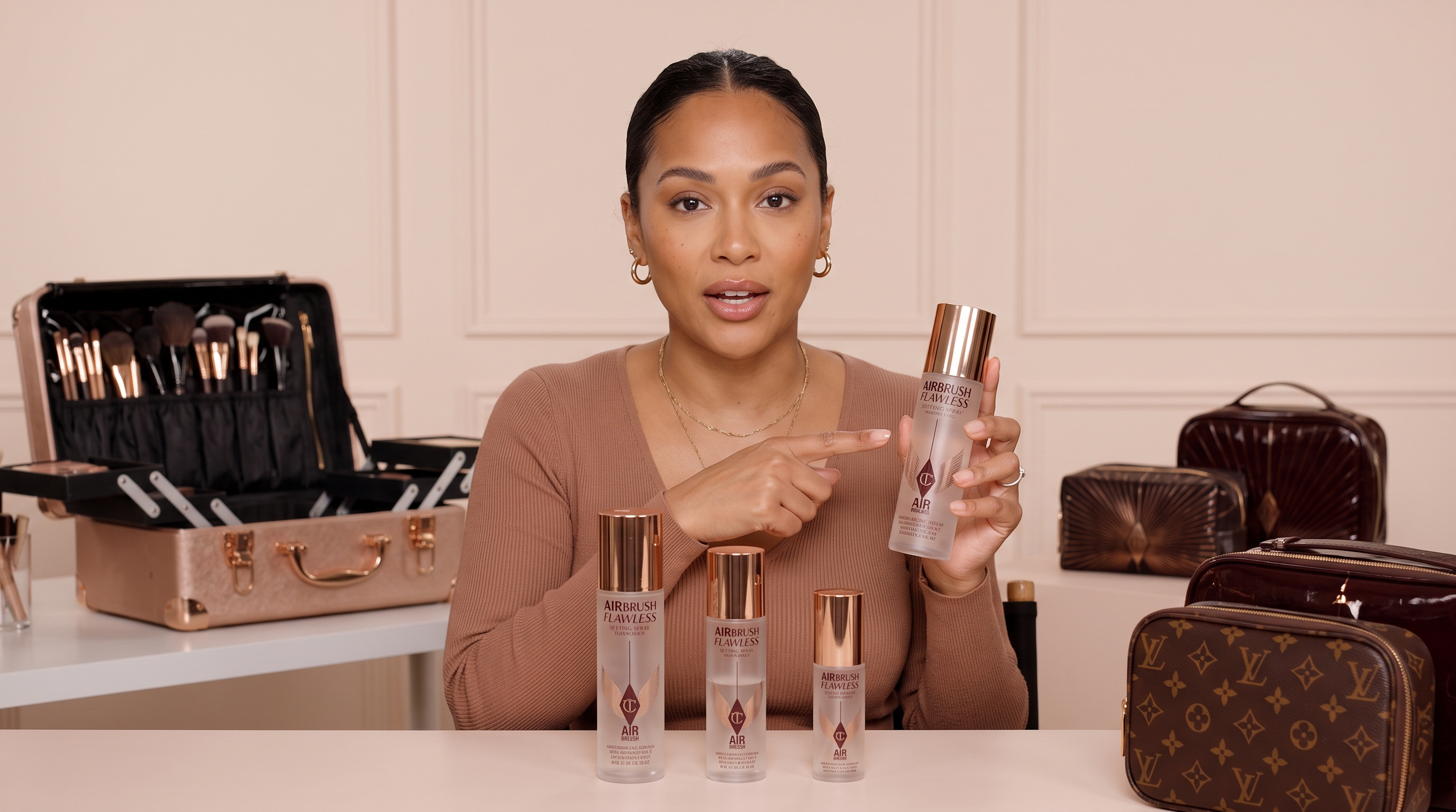 A makeup artist holds and points to Charlotte Tilbury Airbrush Flawless Setting Sprays in 200ml, 100ml, and 34ml bottles.