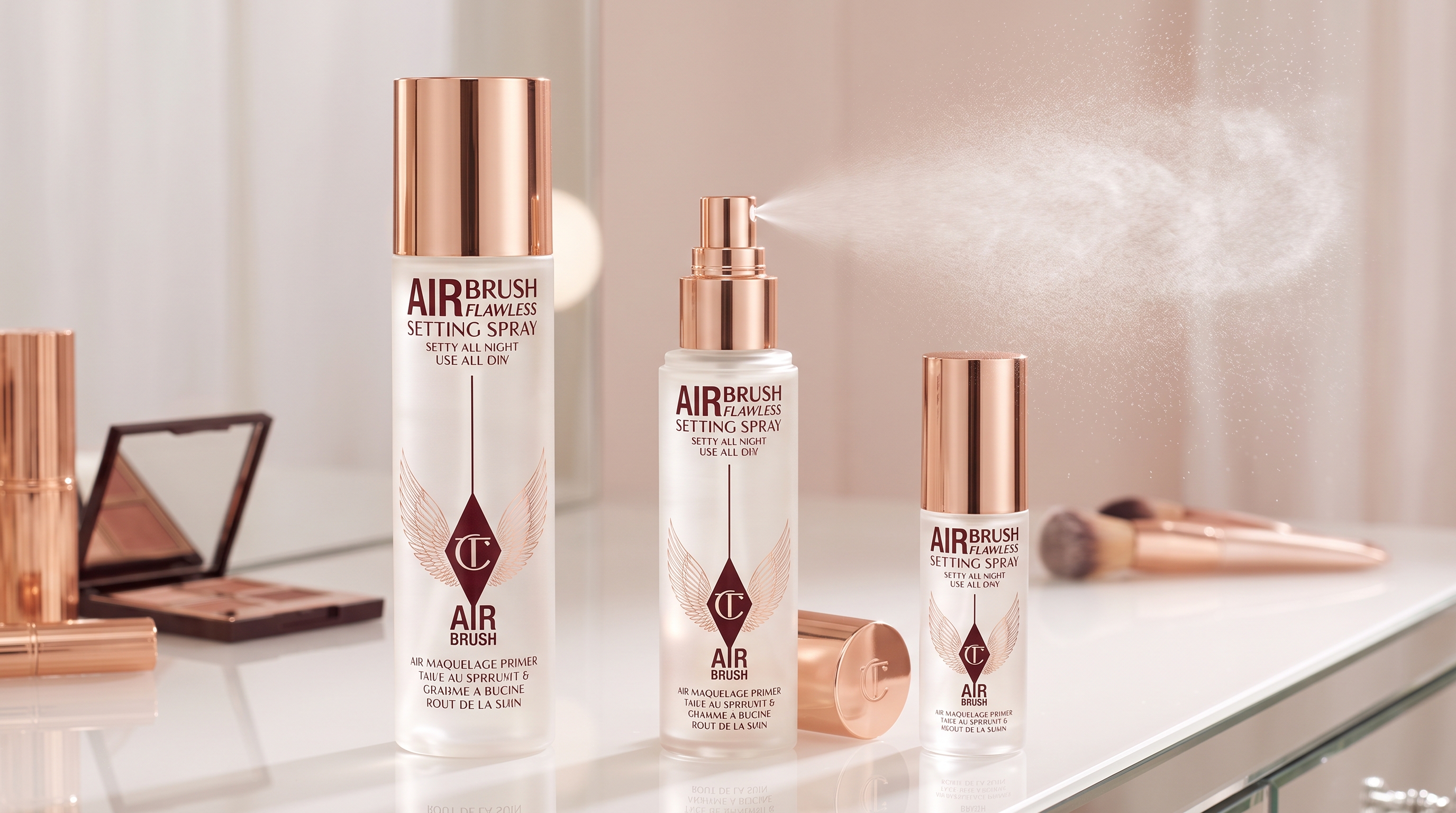 Three sizes of Charlotte Tilbury setting spray bottles on a vanity, with the middle bottle spraying a fine mist.