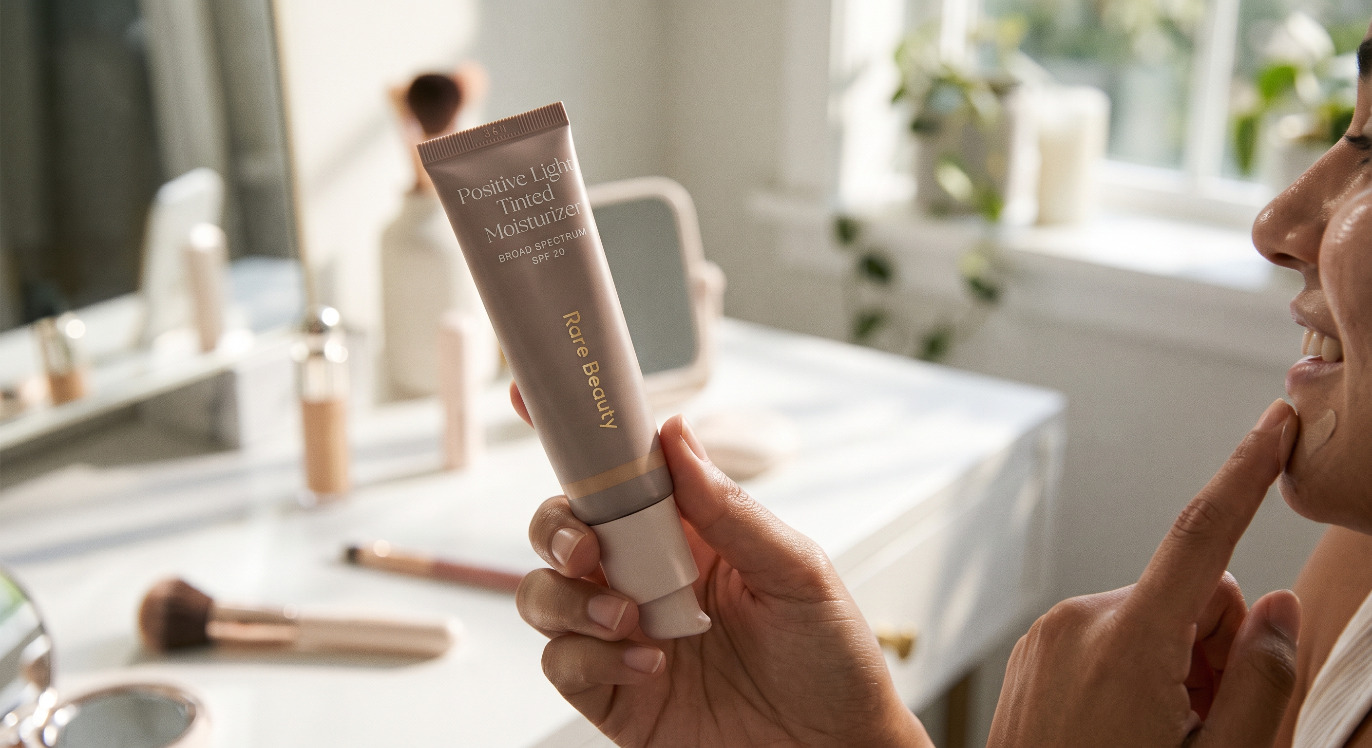 A person holding Rare Beauty Positive Light Tinted Moisturizer while applying a light swatch to their chin.