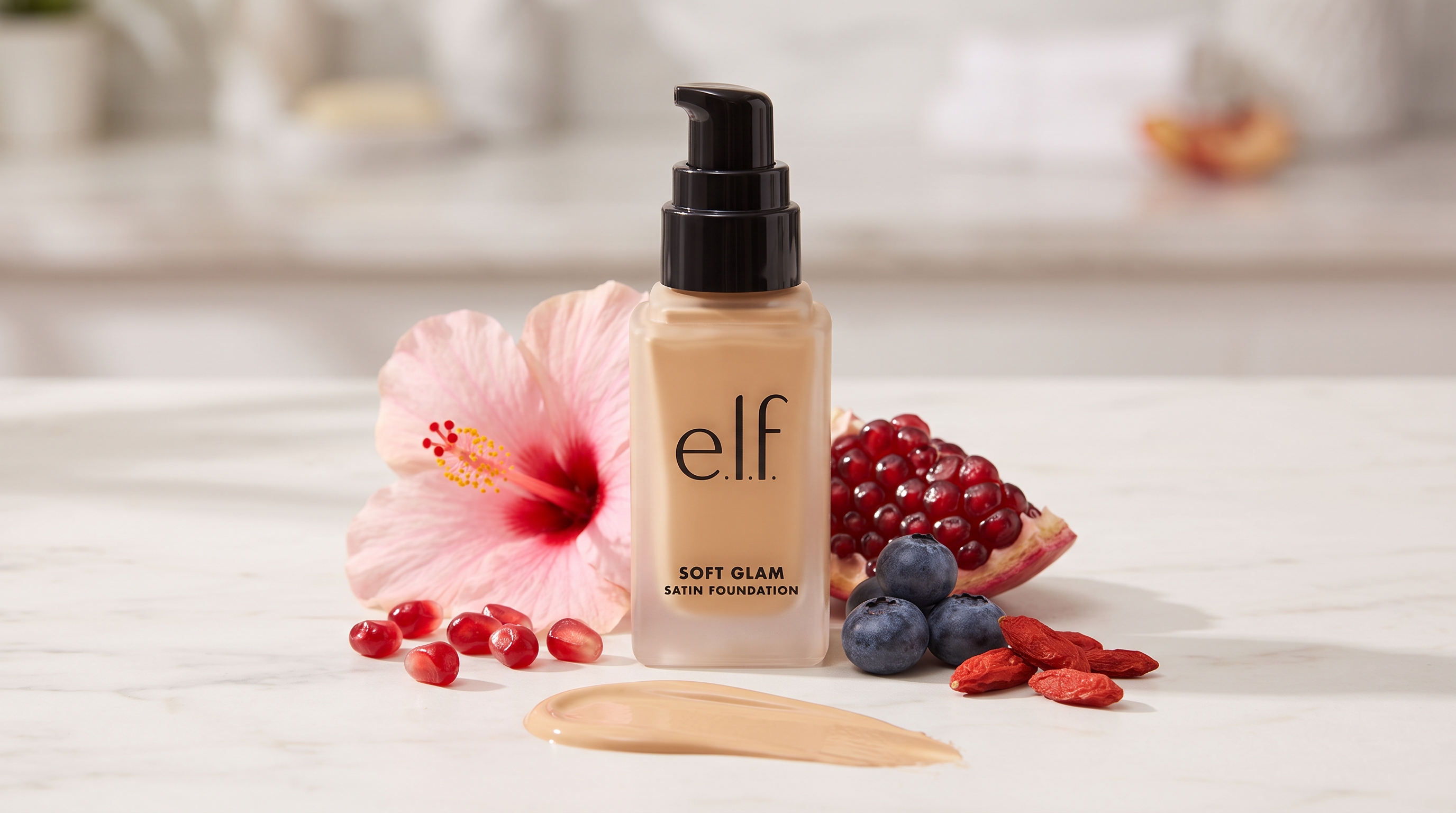 Alt Text: e.l.f. Soft Glam Satin Foundation bottle on a counter with a swatch, hibiscus, pomegranate, blueberries, and goji berries.