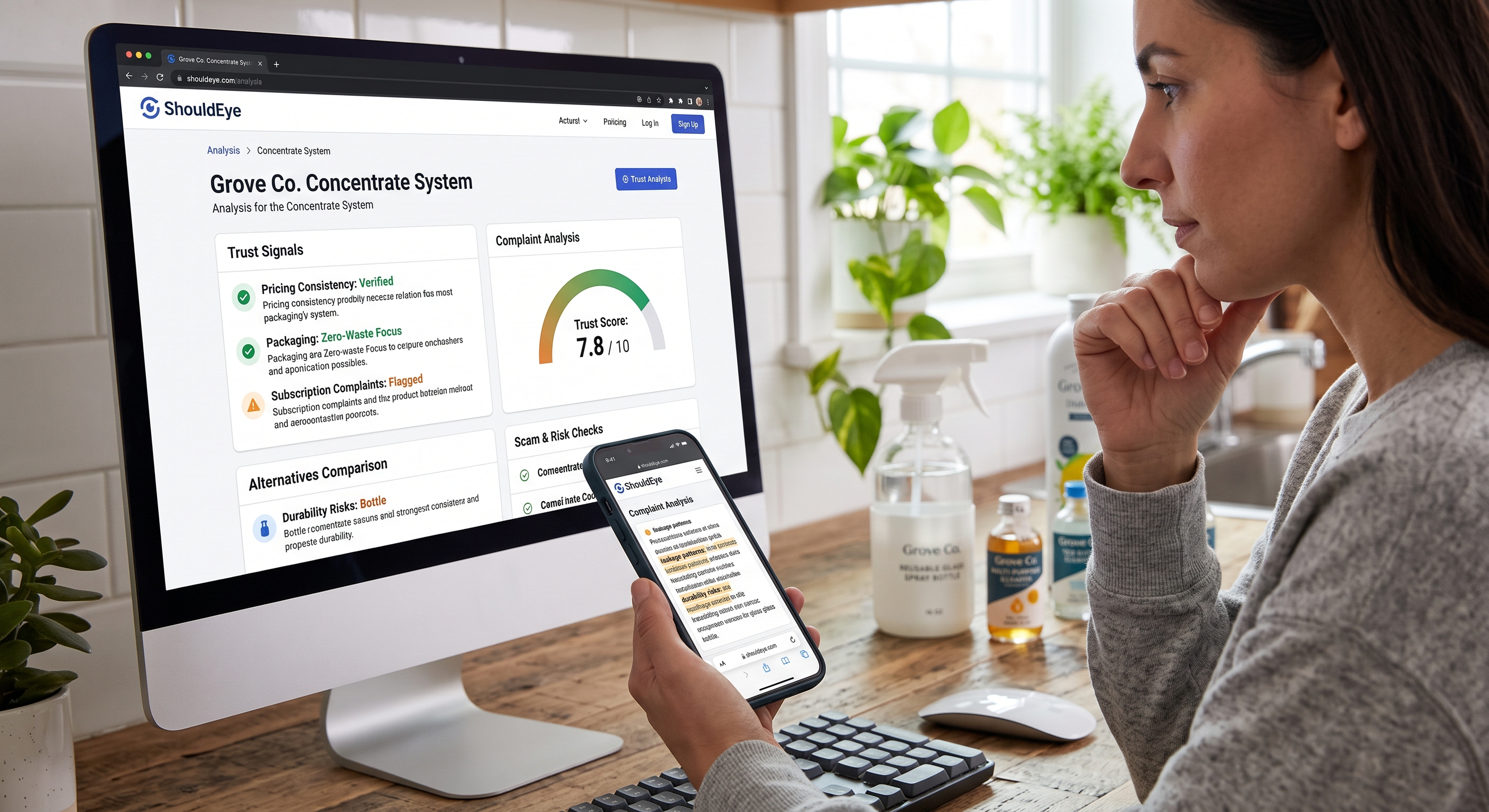 Woman viewing ShouldEye product trust score analysis on desktop computer monitor while holding smartphone.